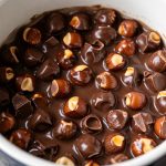 pinterest optimized image of a crockpot filled with glossy chocolate hazelnut candy pieces, showcasing rich texture and nutty bits